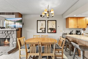 A modern kitchen with a stone fireplace, wooden dining table, and bar area. - Best Of Summit 2025 Winner for Best Lodging Hotel! Premium Slopeside Escape at B (Breckenridge)