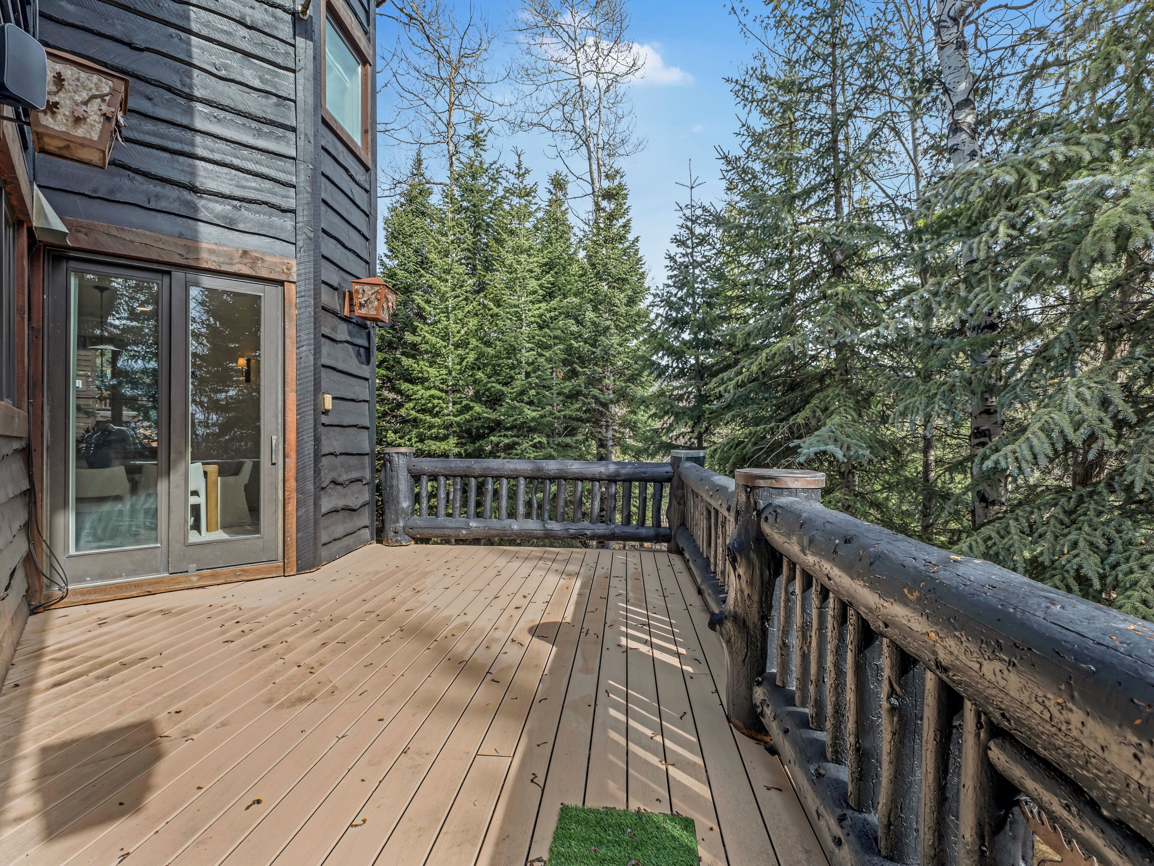 Eine Holzterrasse mit Glastür, die zu einem Raum führt, umgeben von dichtem Wald.