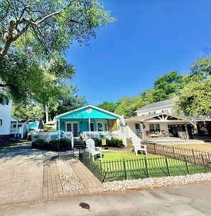 Un quartier résidentiel avec une maison turquoise dotée d’un porche et d’un escalier, entourée d’autres maisons et de verdure.