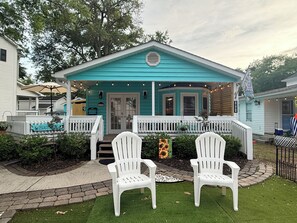 A turquoise house with a porch, two white chairs, and a welcome sign.
