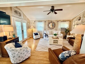 A living room with a sofa, armchairs, a coffee table, a ceiling fan, and a large mirror on the wall.
