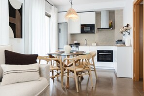 Een moderne keuken met witte kasten, een eethoek met een glazen tafel en houten stoelen, en een hangende lamp.