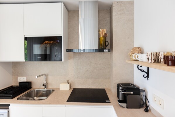 A modern kitchen with a stainless steel sink, a black induction cooktop, a built-in oven, and a black toaster.