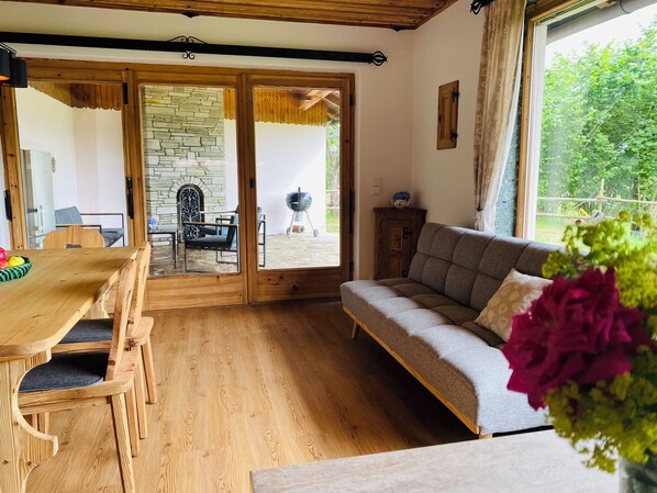 A cozy living room with a wooden dining table, chairs, a sofa, and a stone fireplace.