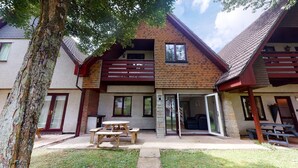 A two-story building with a wooden facade, a balcony, and a patio area with a table and benches.