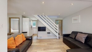 A modern living room with a staircase, a kitchen, and a dining area.