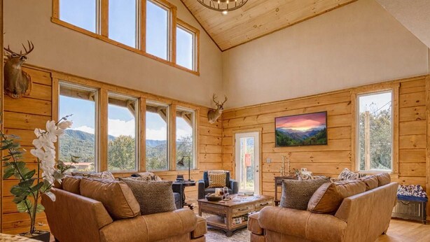 A spacious cabin with large windows, a fireplace, and a mountain view.