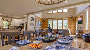 A spacious kitchen with wooden cabinets, a dining area with a long table set for a meal, and a large window providing natural light.