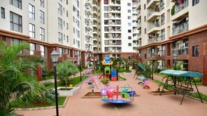 A residential building with multiple balconies, a playground with a swing set, and a small garden area.