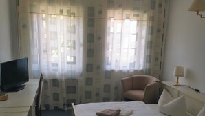 Une chambre d’hôtel avec un lit, un bureau avec un ordinateur, une chaise et une fenêtre avec des rideaux.