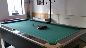 Une table de billard avec des billes, une fenêtre et un porte-manteau.