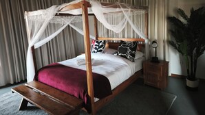 A four-poster bed with a canopy, a wooden nightstand, a potted plant, and a wall-mounted lamp.