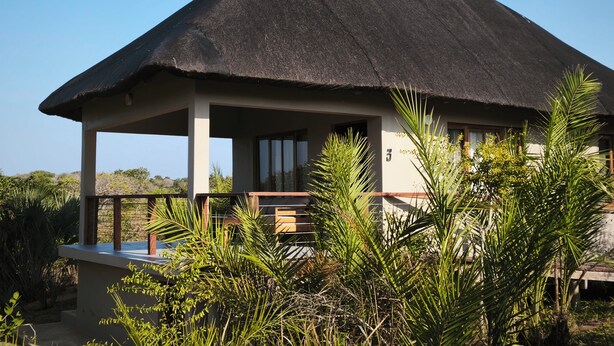 A thatched-roof building with a covered outdoor seating area and lush greenery in the foreground.