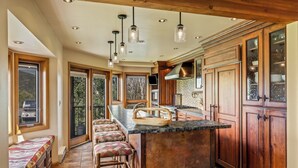 A spacious kitchen with a large island, wooden cabinets, and a stone backsplash. There are multiple bar stools and a built-in bench.