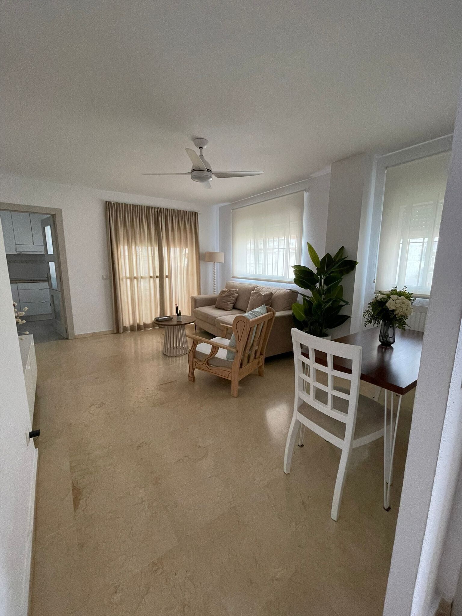 A spacious living room with a sofa, chairs, a dining table, and a ceiling fan.
