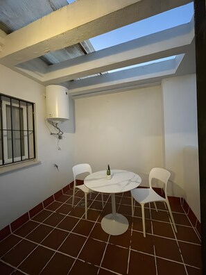 A small, enclosed patio area with a round table and four chairs, a window with bars, and a white air conditioning unit.