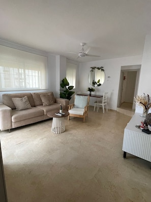 A living room with a sofa, a chair, a small table, a ceiling fan, and a dining area with a chair and table.