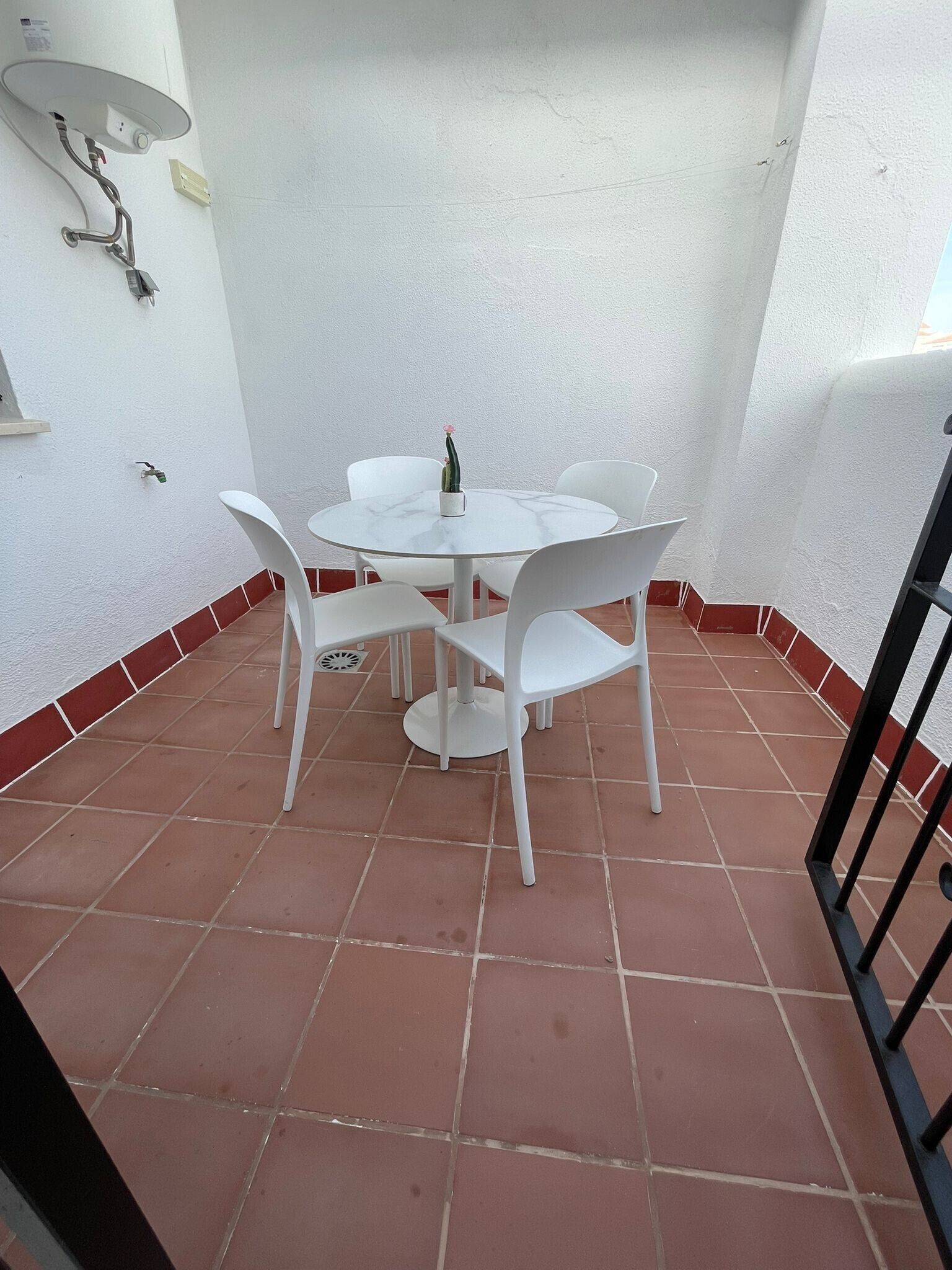 Un pequeño patio amurallado con una mesa redonda y cuatro sillas, una planta en maceta y un aplique de pared.
