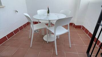 Un pequeño patio amurallado con una mesa redonda y cuatro sillas, una planta en maceta y un aplique de pared.