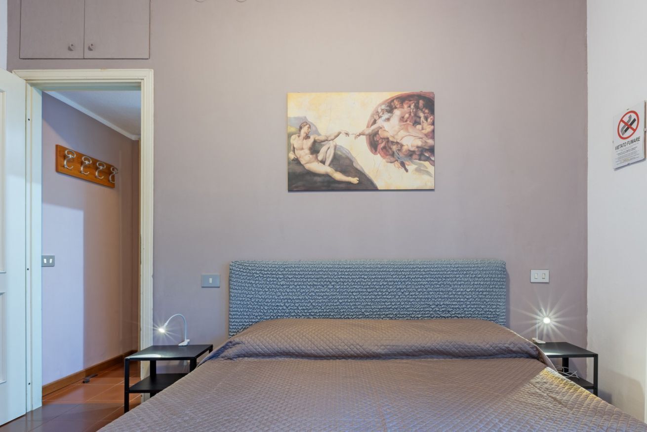 A bedroom with a bed, a wall-mounted painting, a door, and a nightstand.