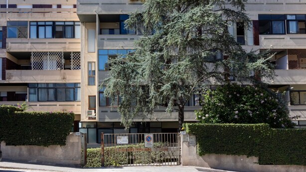 A multi-story residential building with balconies, a tree in the foreground, and a gated entrance. - GuestHost - Hopper House (Cagliari)