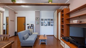 A living room with a sofa, coffee table, TV, and shelves. - GuestHost - Hopper House (Cagliari)