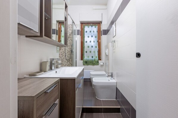 A modern bathroom with a wooden vanity, a large mirror, a sink, a bidet, and a shower.