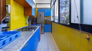 A narrow kitchen with blue and yellow cabinets, a stainless steel stove, and a view through a window. - GuestHost - Hopper House (Cagliari)