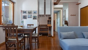 A living room with a sofa, dining table, chairs, and a kitchen area with cabinets and a water dispenser. - GuestHost - Hopper House (Cagliari)