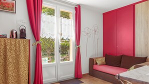 Una habitación con un sofá, una mesa, un aparador estampado y una ventana con cortinas.