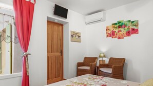 Un dormitorio con una cama, dos sillas de mimbre, un televisor y un aire acondicionado instalado en la pared.