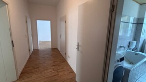 A hallway with wooden flooring leading to a bathroom with a sink and washing machine. - Large flat with separate rooms for 8 guests STPh (Zeitz)