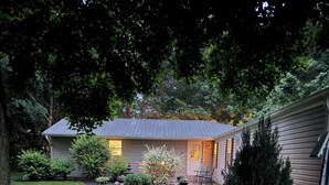 Ein Haus mit überdachter Veranda, Rasen und Garten mit verschiedenen Pflanzen und einem Weg.