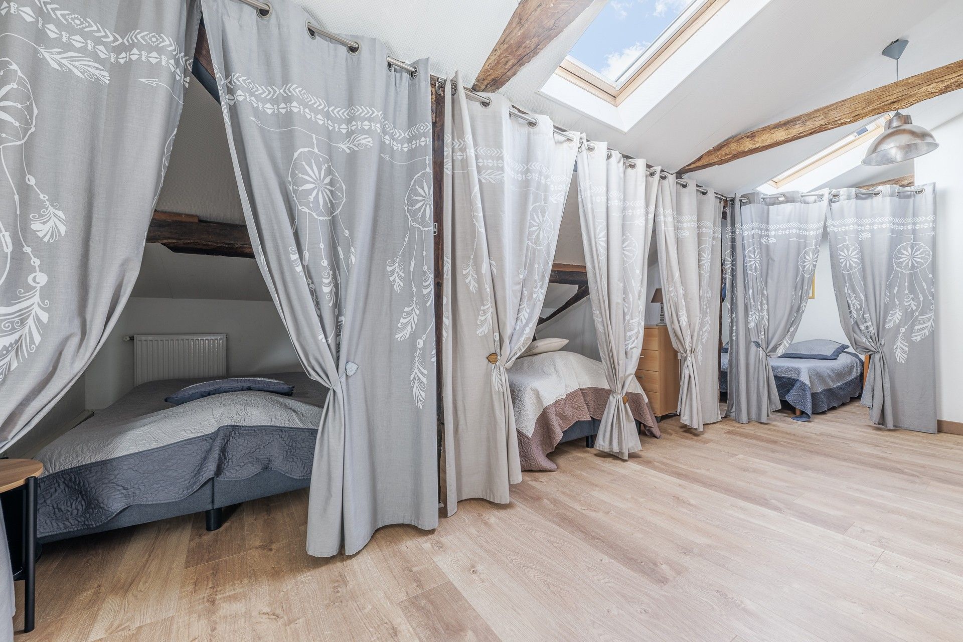 Ein Schlafzimmer mit Oberlicht, zwei Betten und grauen Vorhängen mit Blätermotiv.