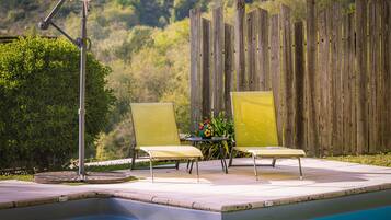 A poolside area with two yellow chairs, a table with a flower vase, and a wooden fence in the background.