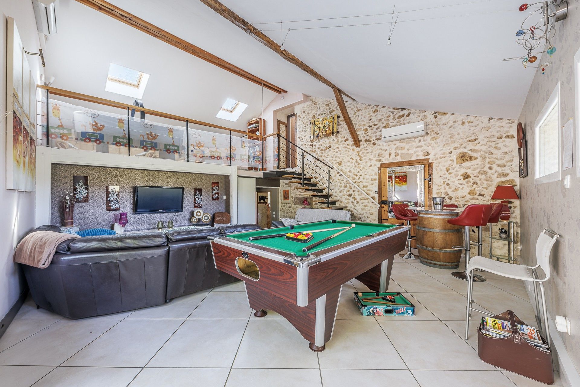 A spacious living area with a pool table, a sofa, and a staircase leading to an upper level.