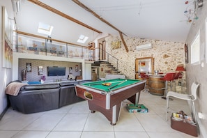 Un vaste espace de vie comprenant une table de billard, un canapé et un escalier menant à un niveau supérieur.