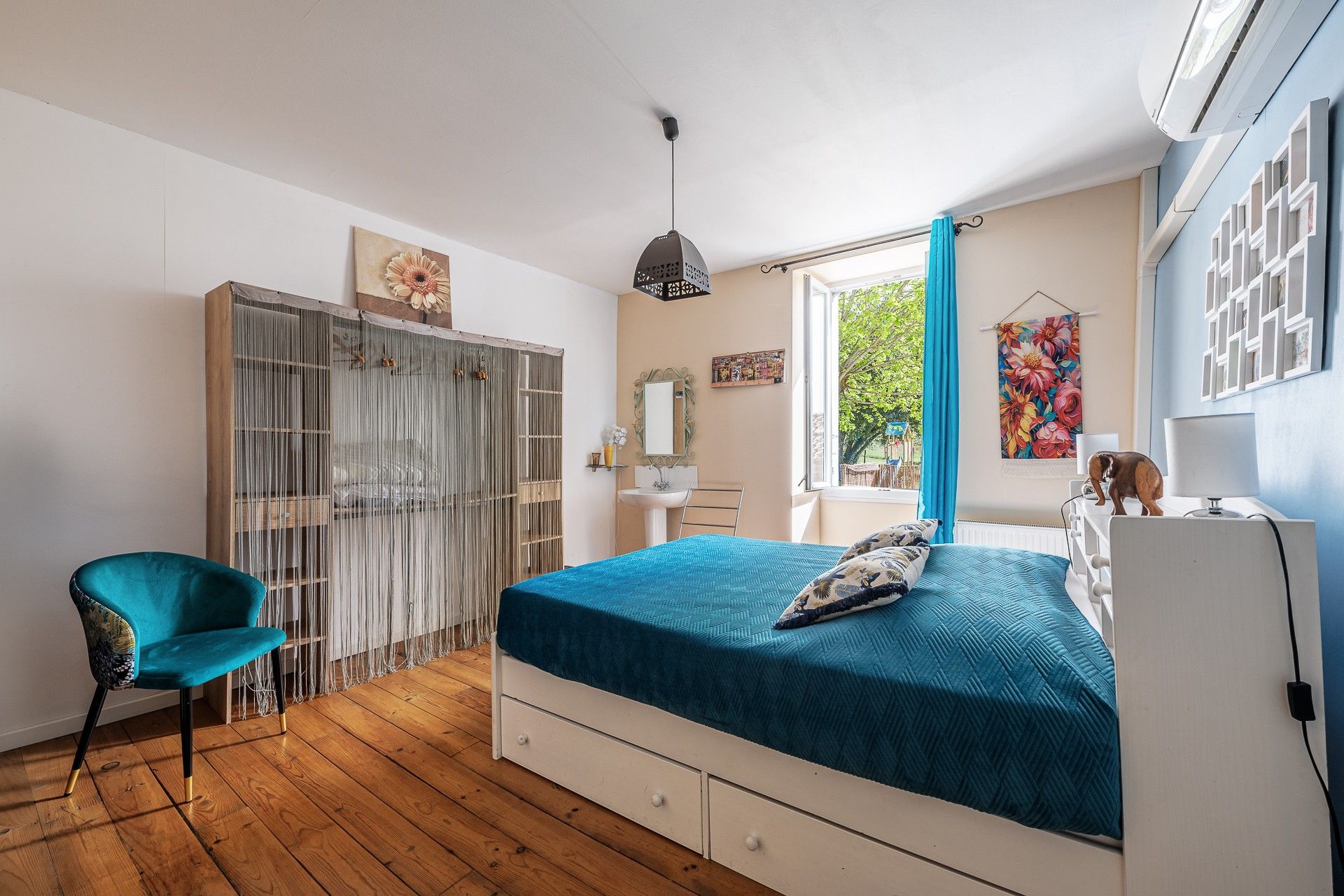 Ein Schlafzimmer mit einem Bett, einem Sessel, einem Kleiderschrank, einem Fenster und einem an der Wand befestigten Regal.