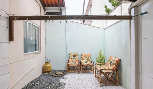 A small, enclosed outdoor space with a gravel floor, two wooden chairs with floral cushions, and a yellow gas cylinder.