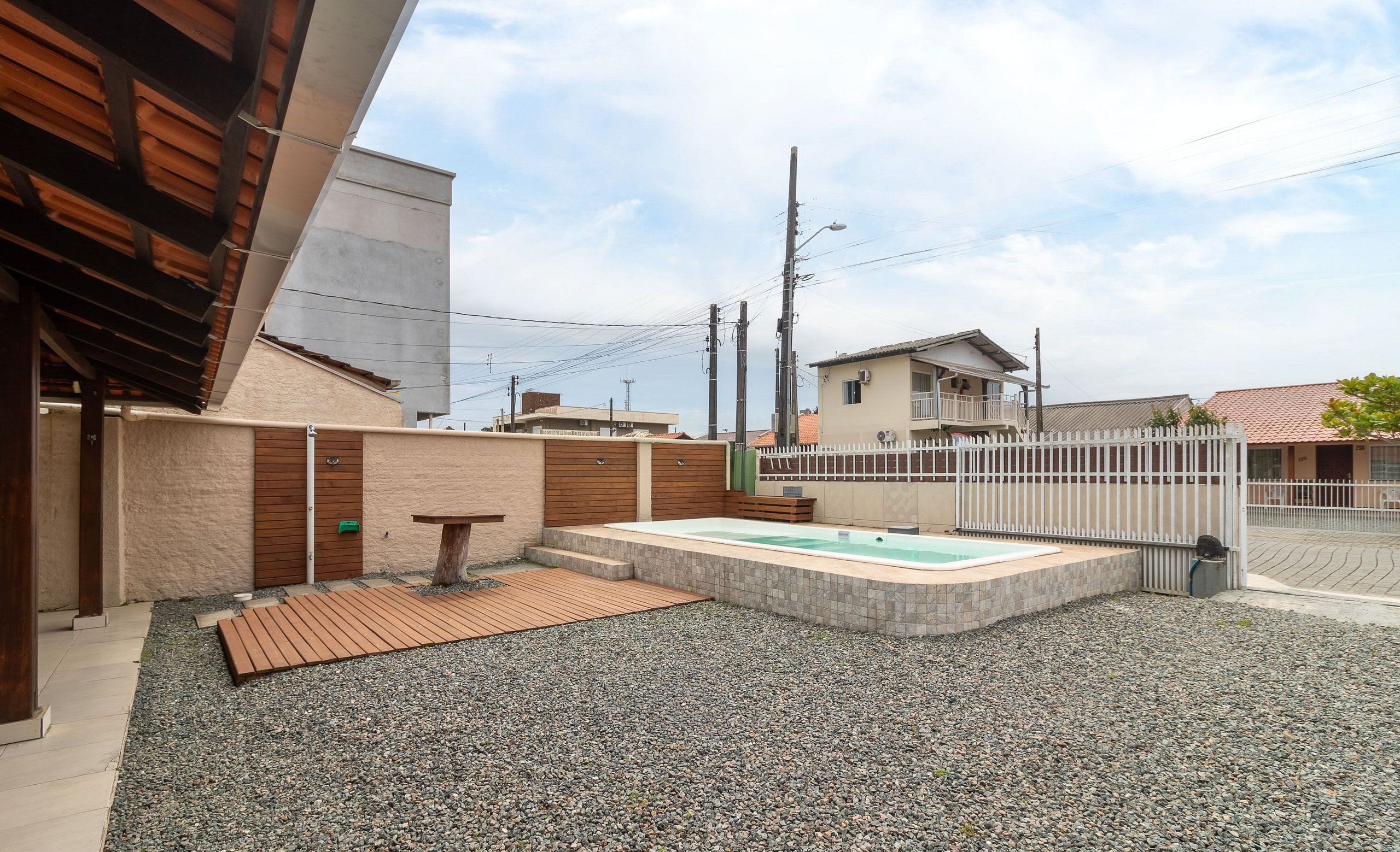 A modern outdoor area with a hot tub, wooden deck, and a gravel ground.