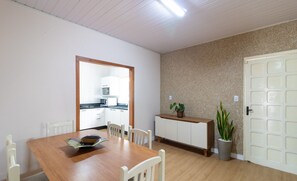 A dining area with a wooden table and white chairs, a kitchen in the background, and a potted plant near the door. - 4 BR House w/ Pool, 500m From Beto Carrero Jrs0130 (Penha)