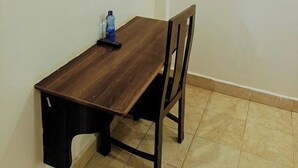 Una habitación pequeña y sencilla, con una mesa y sillas de madera, un televisor de pantalla plana en la pared y suelo de baldosas.