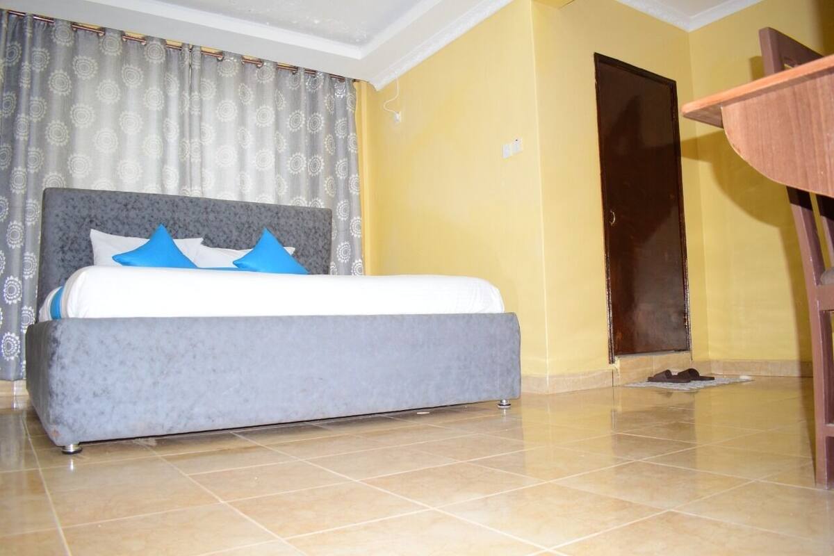 A bedroom with a large bed, a wooden chair, a door, and a patterned curtain.