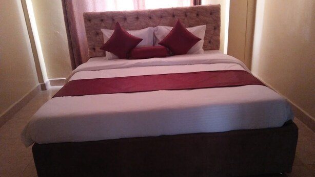 Una cama bien hecha con cabecera de madera, ropa de cama blanca y roja, y una manta roja.