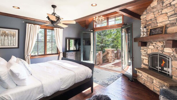 Ein Schlafzimmer mit einem Bett, einem Deckenventilator, einem Kamin aus Stein und Blick ins Freie.