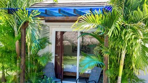 A covered outdoor seating area with two chairs, surrounded by lush tropical plants and a glass door leading to a shaded interior space. - SOSUA Luxury 9-BDR Villa : 20 Guests : POOL (Sosúa)