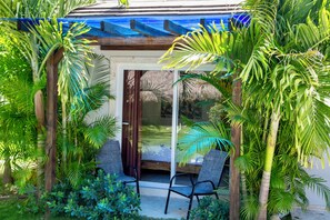 A covered outdoor seating area with two chairs, surrounded by lush tropical plants and a glass door leading to a shaded interior space. - SOSUA Luxury 9-BDR Villa : 20 Guests : POOL (Sosúa)