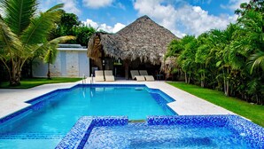 A swimming pool with blue mosaic tiles, surrounded by palm trees and a thatched-roof building. - SOSUA Luxury 9-BDR Villa : 20 Guests : POOL (Sosúa)