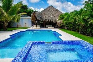 A swimming pool with blue mosaic tiles, surrounded by palm trees and a thatched-roof building. - SOSUA Luxury 9-BDR Villa : 20 Guests : POOL (Sosúa)