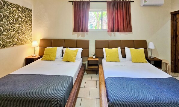 A hotel room with two beds, each with a headboard, bedside tables, lamps, and a window with curtains.